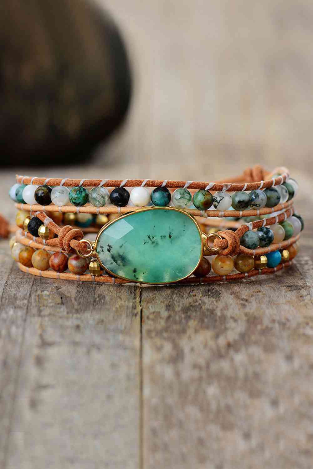 A modern layered bracelet features a large turquoise-green natural stone centerpiece, multicolored agate beads, and wrapped tan cord construction.