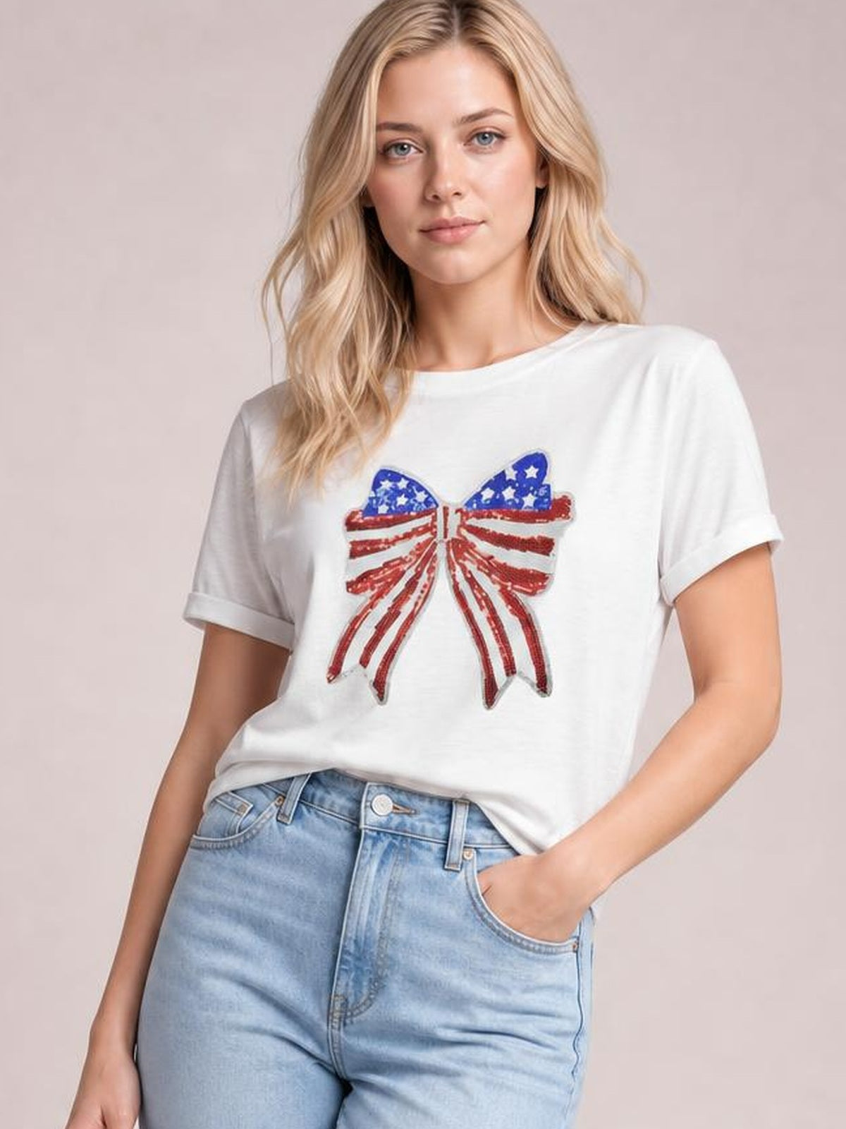 Model poses in a white crew neck T-shirt with rolled sleeves and a sparkling sequin USA flag bow knot patch, styled in a relaxed silhouette.