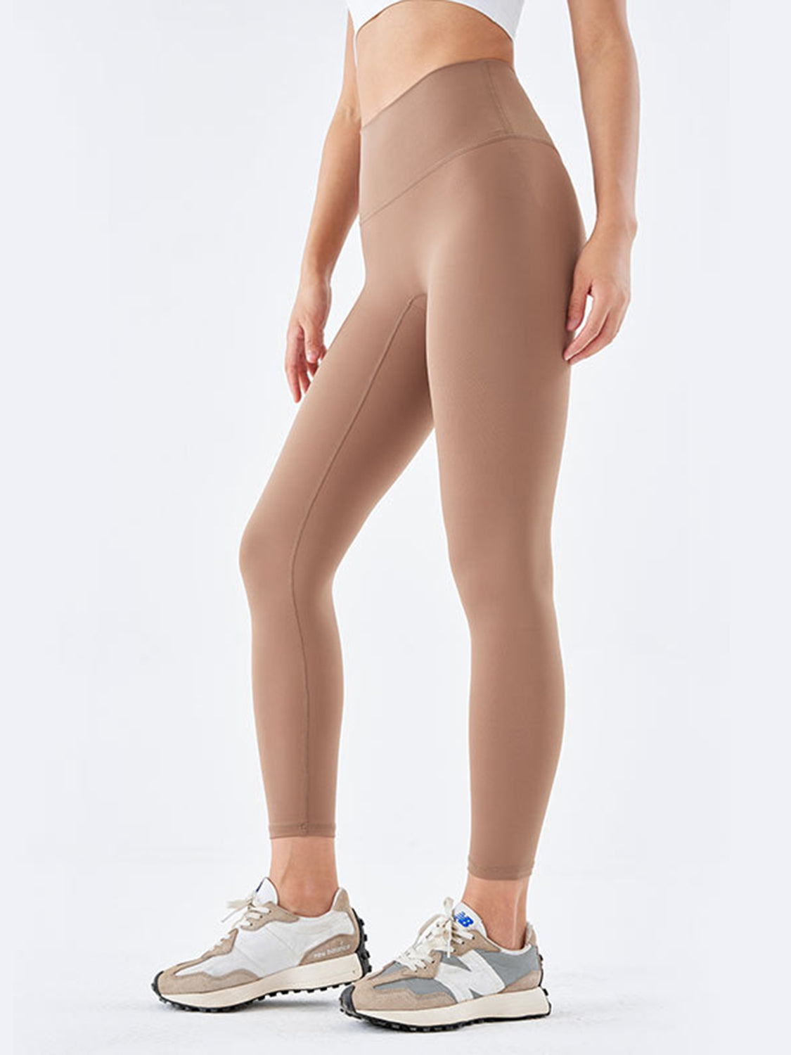 Model wears tan wide waistband sports leggings with a high-rise fit, full-length silhouette, and visible seams while standing with one leg slightly bent.