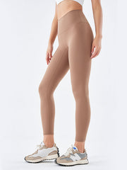 Model wears tan wide waistband sports leggings with a high-rise fit, full-length silhouette, and visible seams while standing with one leg slightly bent.