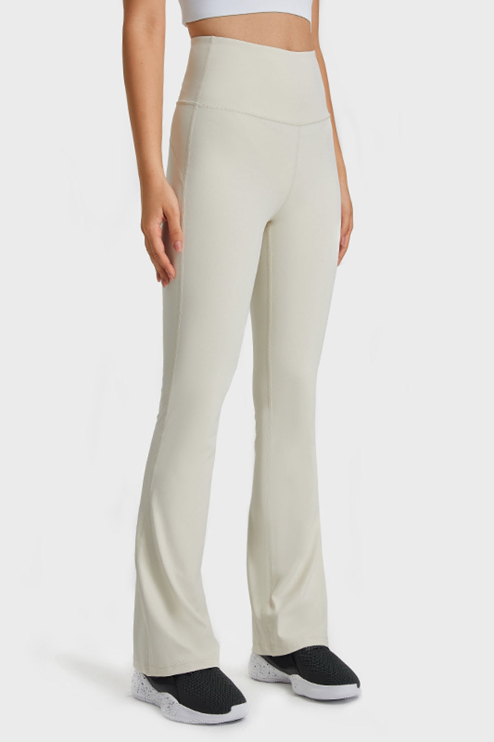 Model stands in cream solid yoga pants with a high elastic waist, smooth stretch fabric, seamed construction, fitted hips and long flared legs.