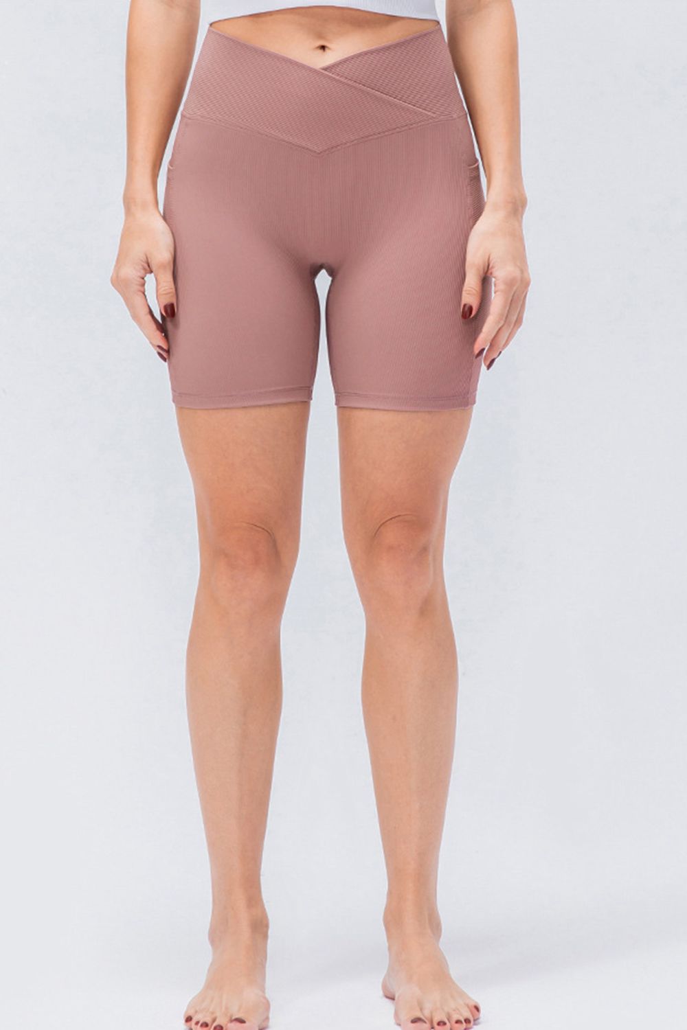Model standing with hands at her sides wears mauve slim-fit sports shorts featuring a high V-waistband, stretch construction, and above-knee silhouette.