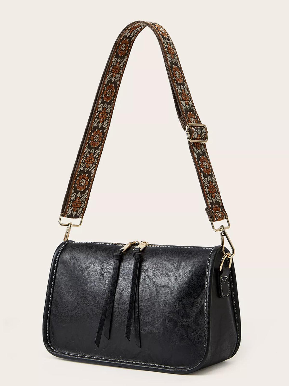 Small black PU leather vintage-style crossbody bag with a patterned adjustable strap, rounded rectangular silhouette, front tie details, and gold-tone hardware.
