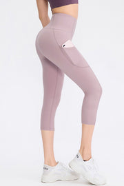 Model poses in mauve cropped active leggings with a wide waistband, slim-fit silhouette, curved seams, and a side pocket holding a phone.