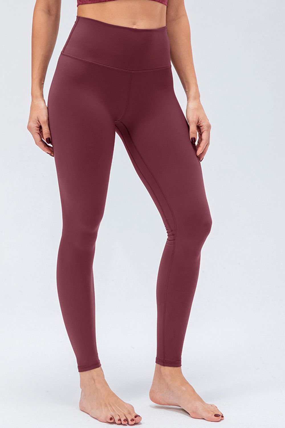 Model wearing burgundy solid active leggings with a wide waistband, slim fit, ankle-length silhouette, and smooth seamed construction.