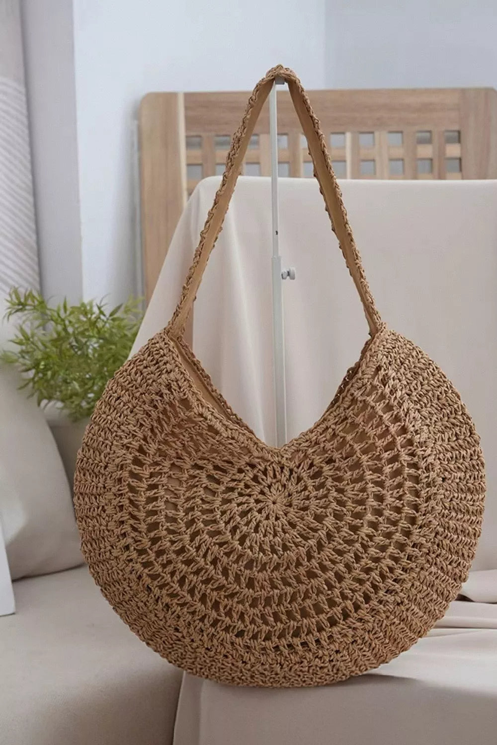 Medium tan round woven shoulder bag with an openwork crochet-style construction, slouchy silhouette, and long braided strap.