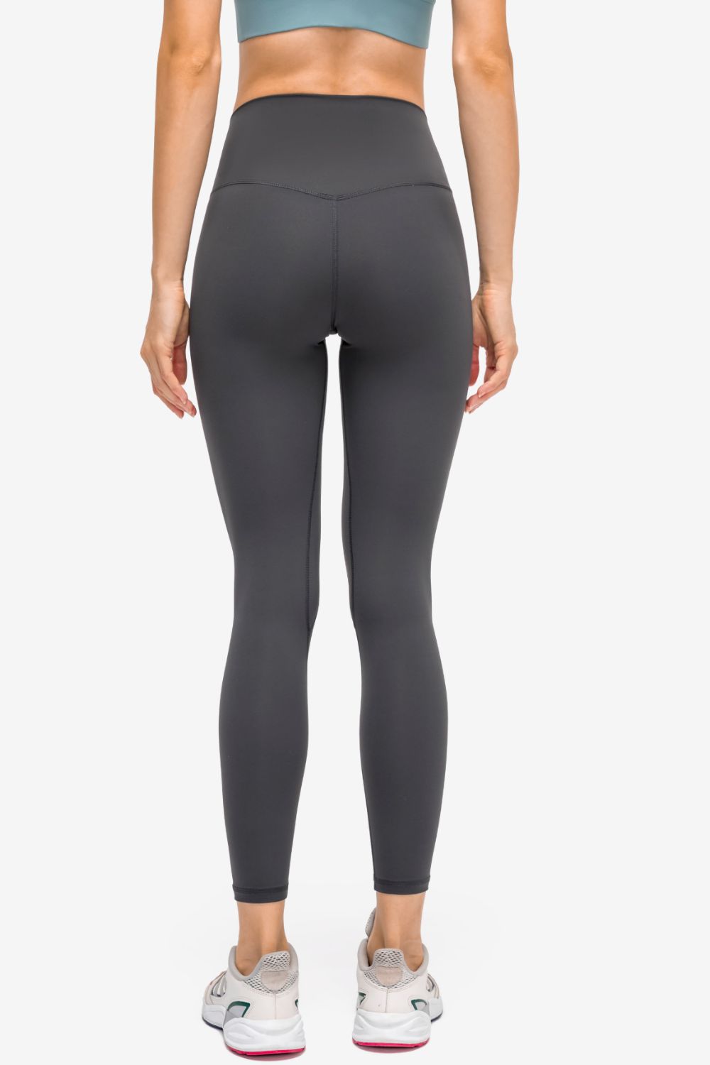 Rear view of a model wearing solid black high-rise sports leggings with a slim, sculpted silhouette, matte stretch fabric, and visible seam construction.