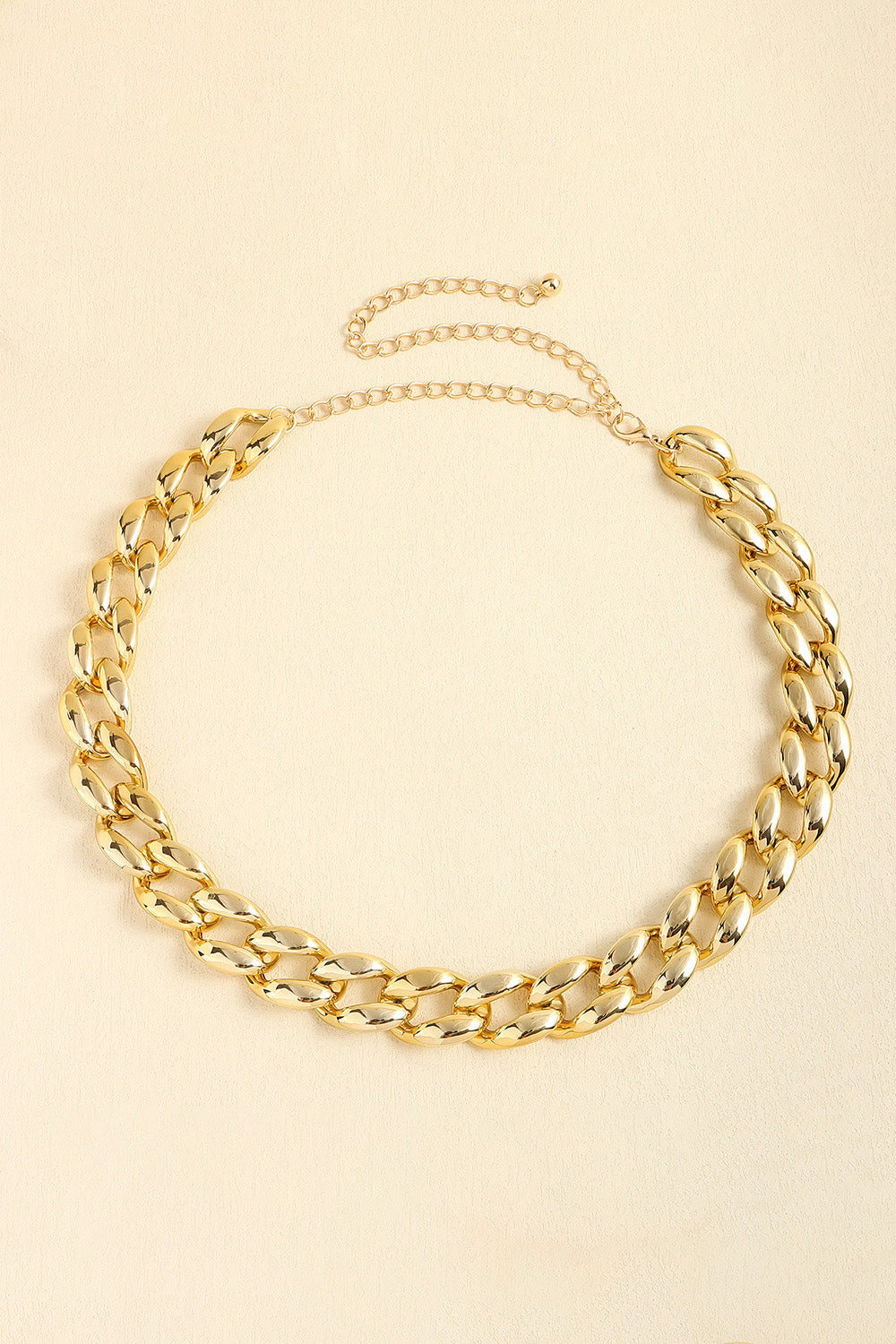 A polished gold acrylic curb chain belt is shown flat, featuring bold interlocking links, a 1-inch width, and an adjustable extension chain with clasp.