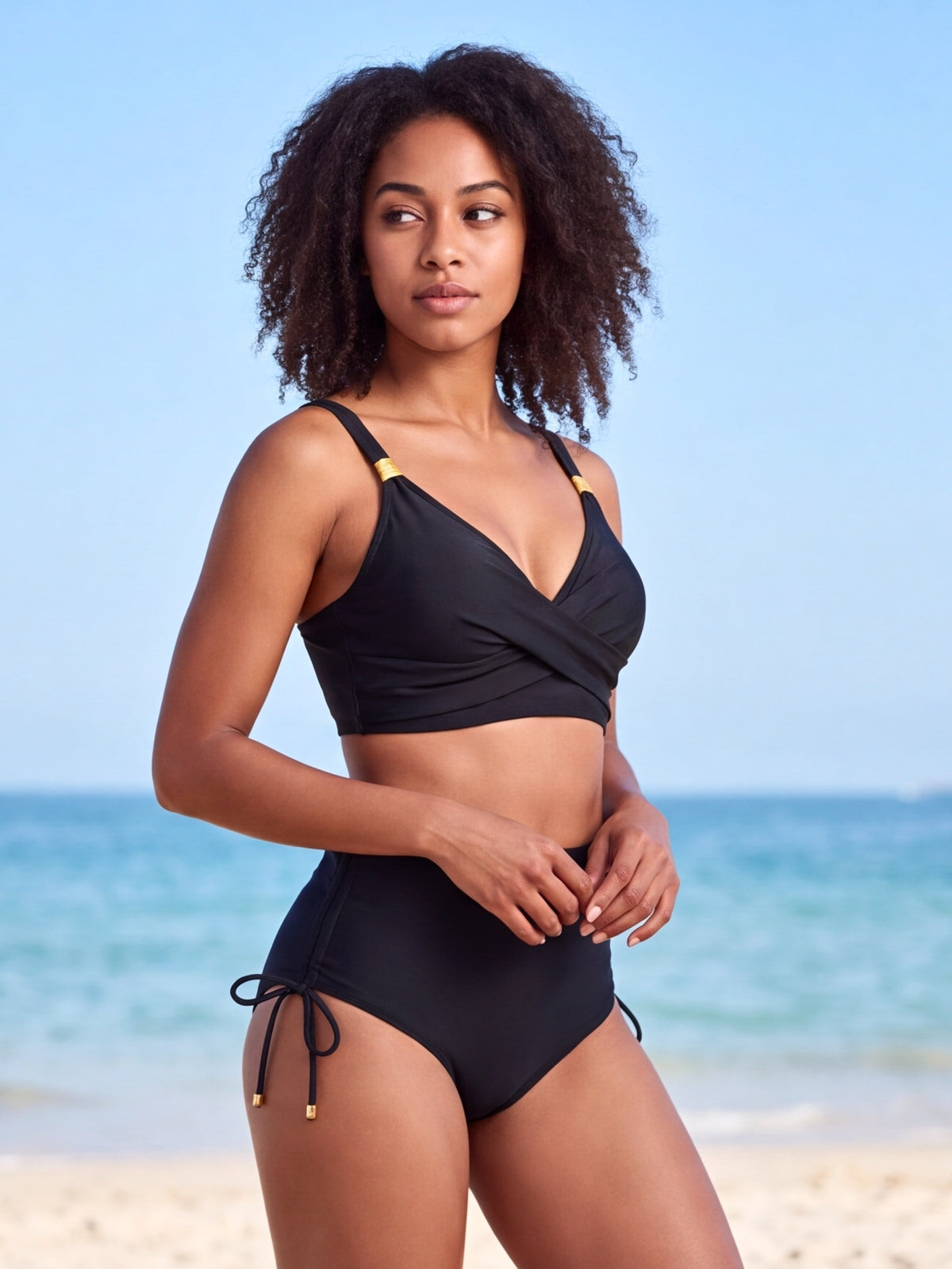 Model poses in a black crisscross high-waisted swim set with wrap-style top, shoulder straps, and side-tie bikini bottoms.