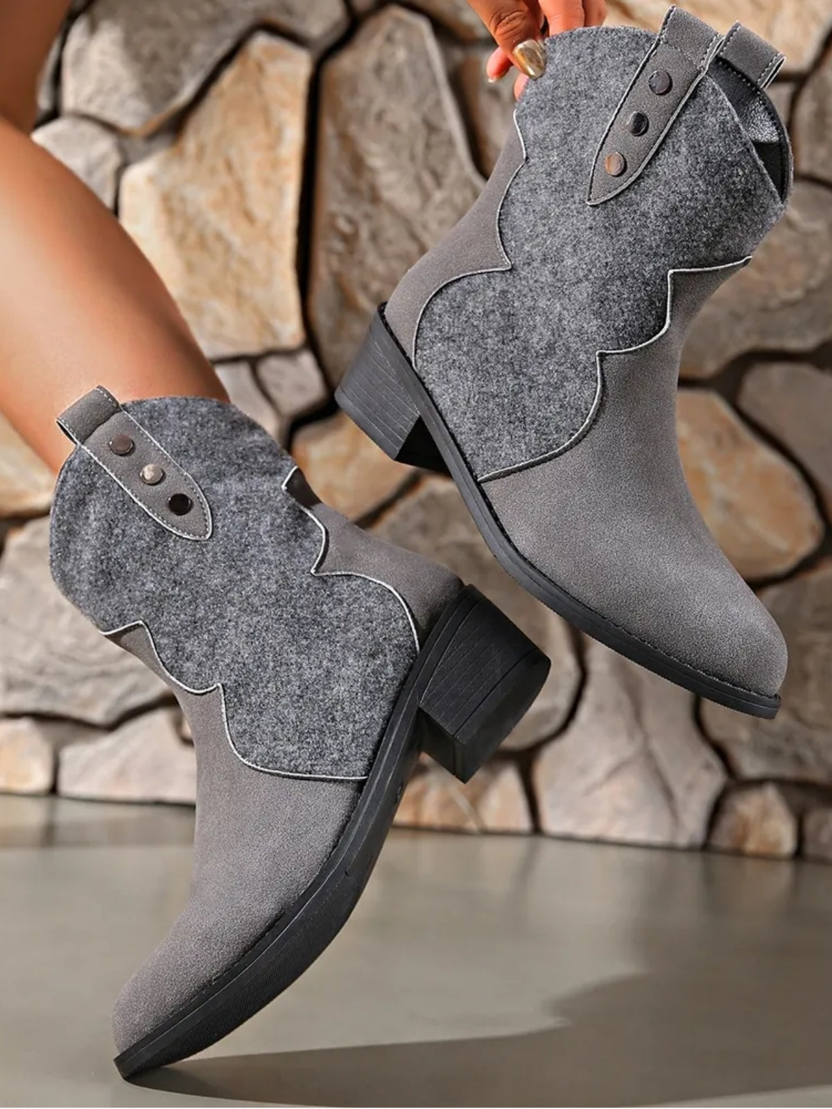 A model displays gray suede point-toe boots with low block heels, scalloped shaft panels, and decorative buttoned straps.