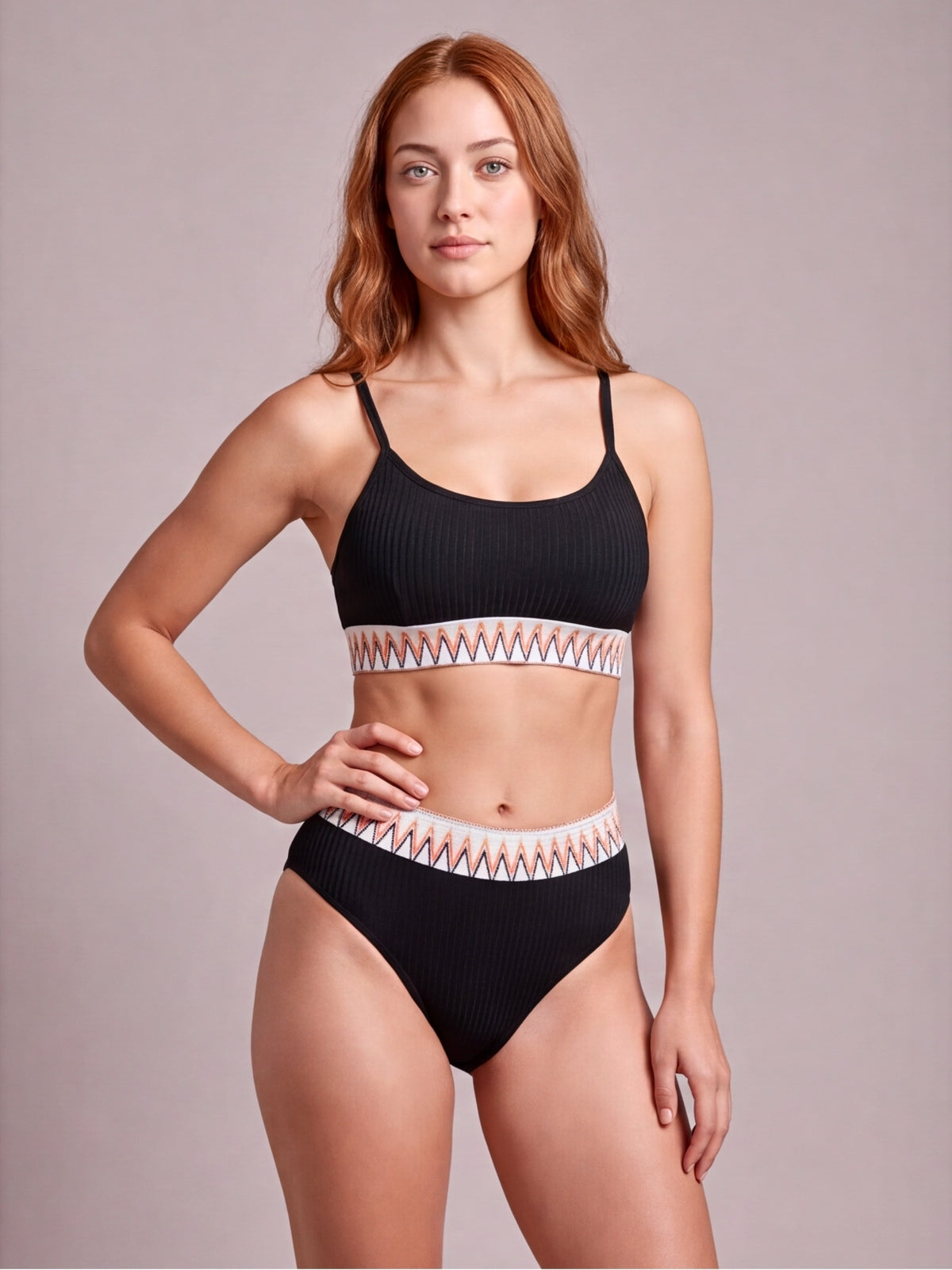 Model poses in a black textured ribbed high-waist bikini with contrast geometric banding on the scoop-neck top and waistband.