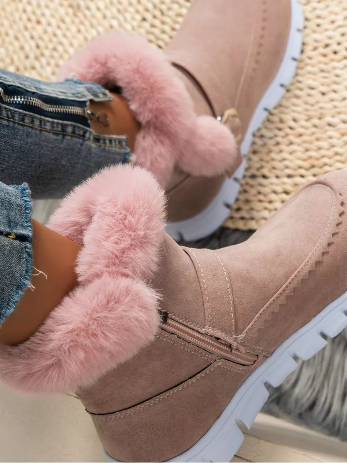 A model wears taupe suede flat boots with plush pink fuzzy trim, side buckle straps, stitched panels, and white rubber lug soles.