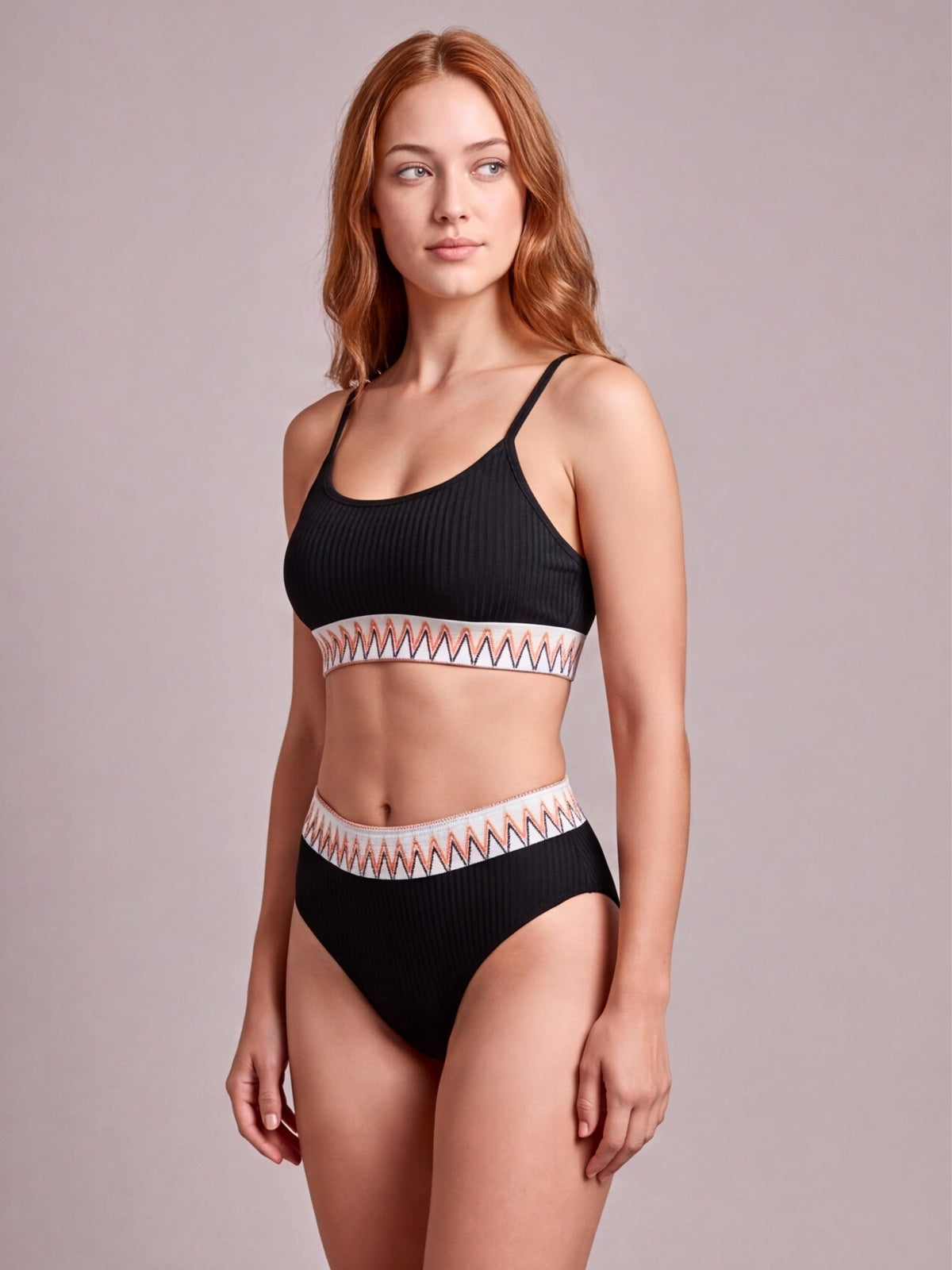Model poses in a black textured bikini with thin straps, a patterned contrast band, and high-waisted bottoms creating a supportive two-piece silhouette.