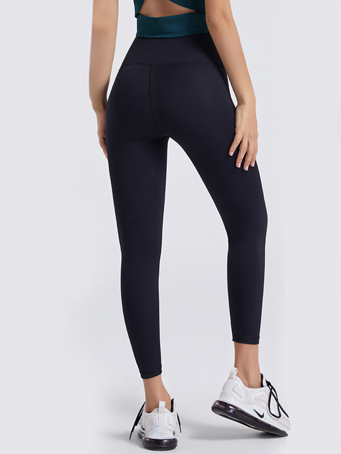 Model shown from behind in black wide-waistband sports leggings with a high-rise, close-fitting silhouette, ankle-length legs, and visible seam construction.