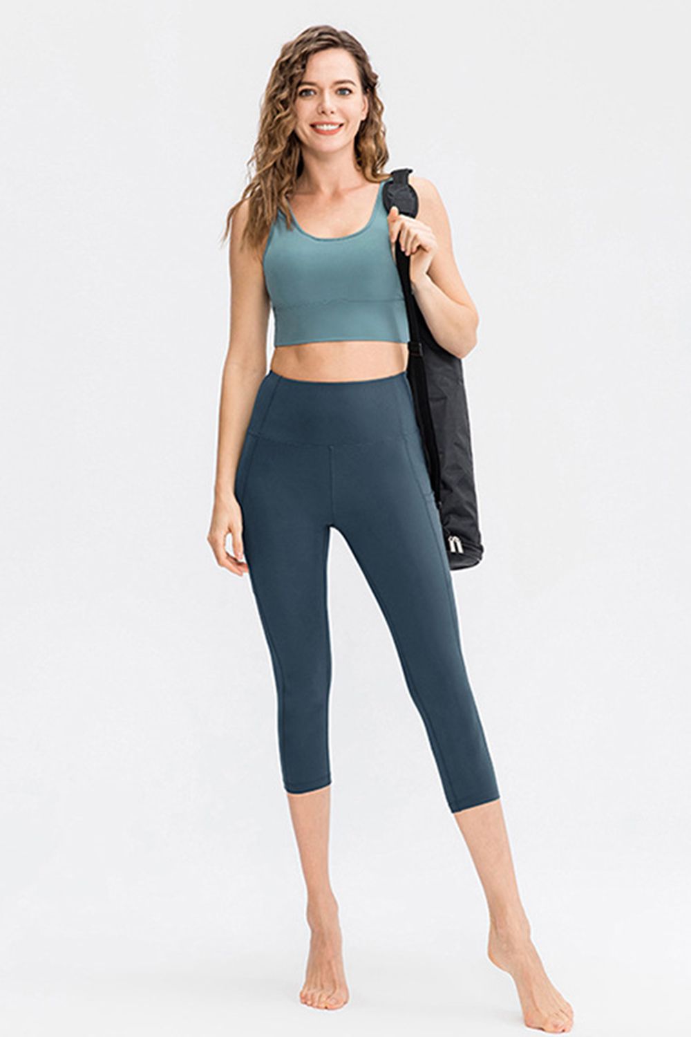 Model standing in a relaxed pose wears solid navy cropped active leggings with a wide waistband, slim-fit silhouette, and visible side pocket construction.