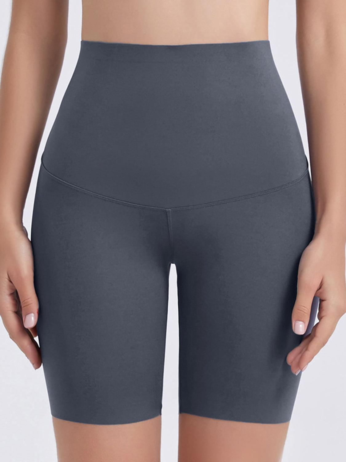 Model wears charcoal gray wide waistband sports shorts with a smooth fitted silhouette, mid-thigh length, curved seam, and hands resting at the sides.