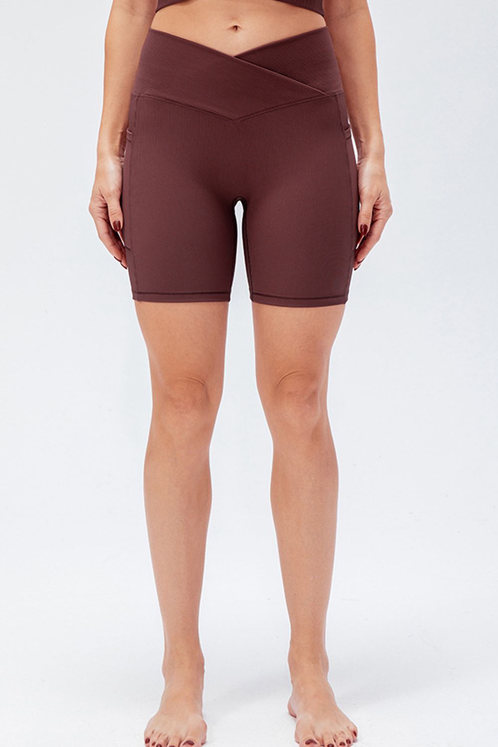 Model stands with hands at her sides wearing solid brown slim-fit sports shorts with a V-waistband and close-fitting, knee-length silhouette.