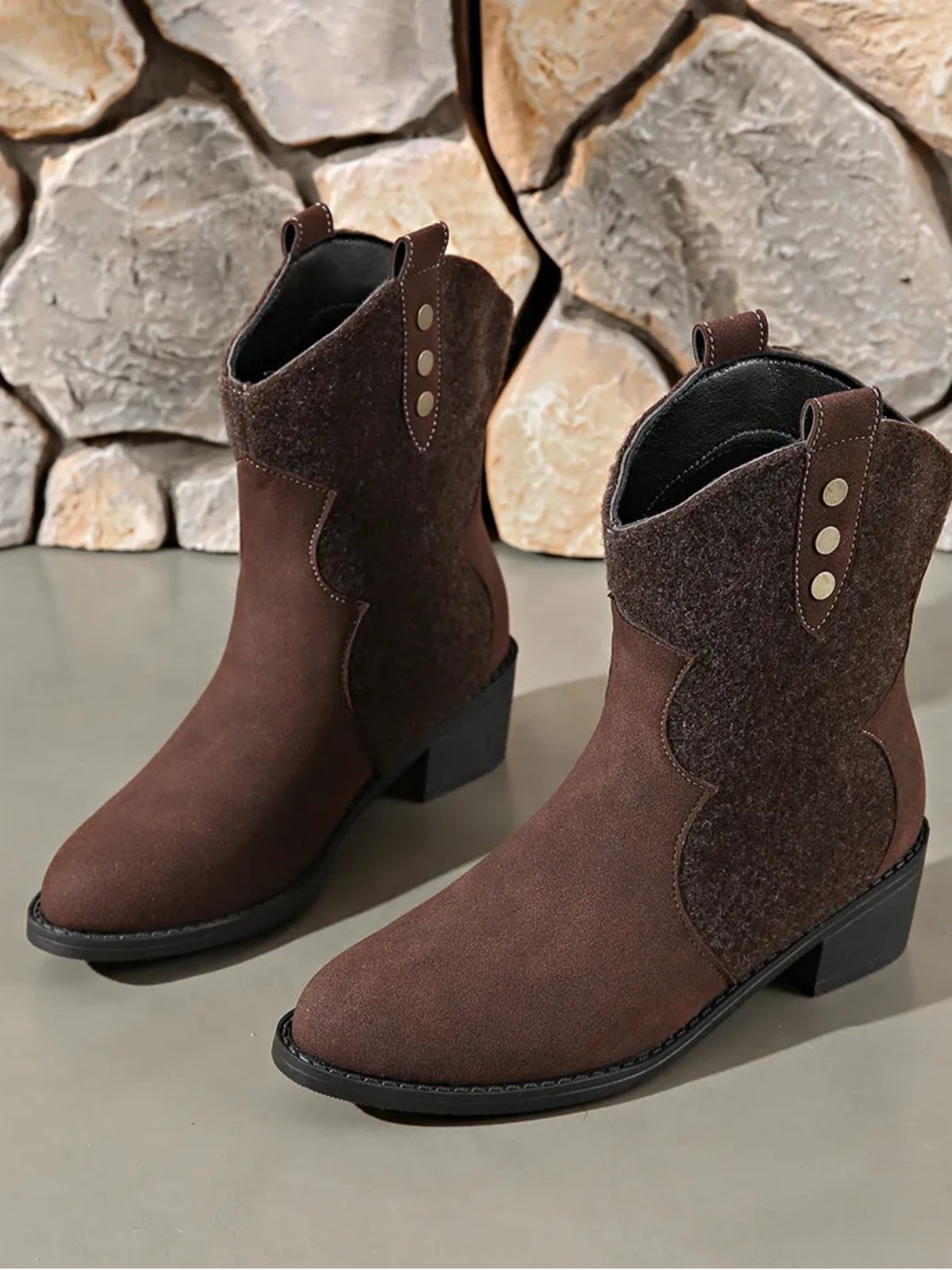 Brown suede point-toe boots feature contrast paneling, pull tabs, decorative stud details, black soles, and low block heels.
