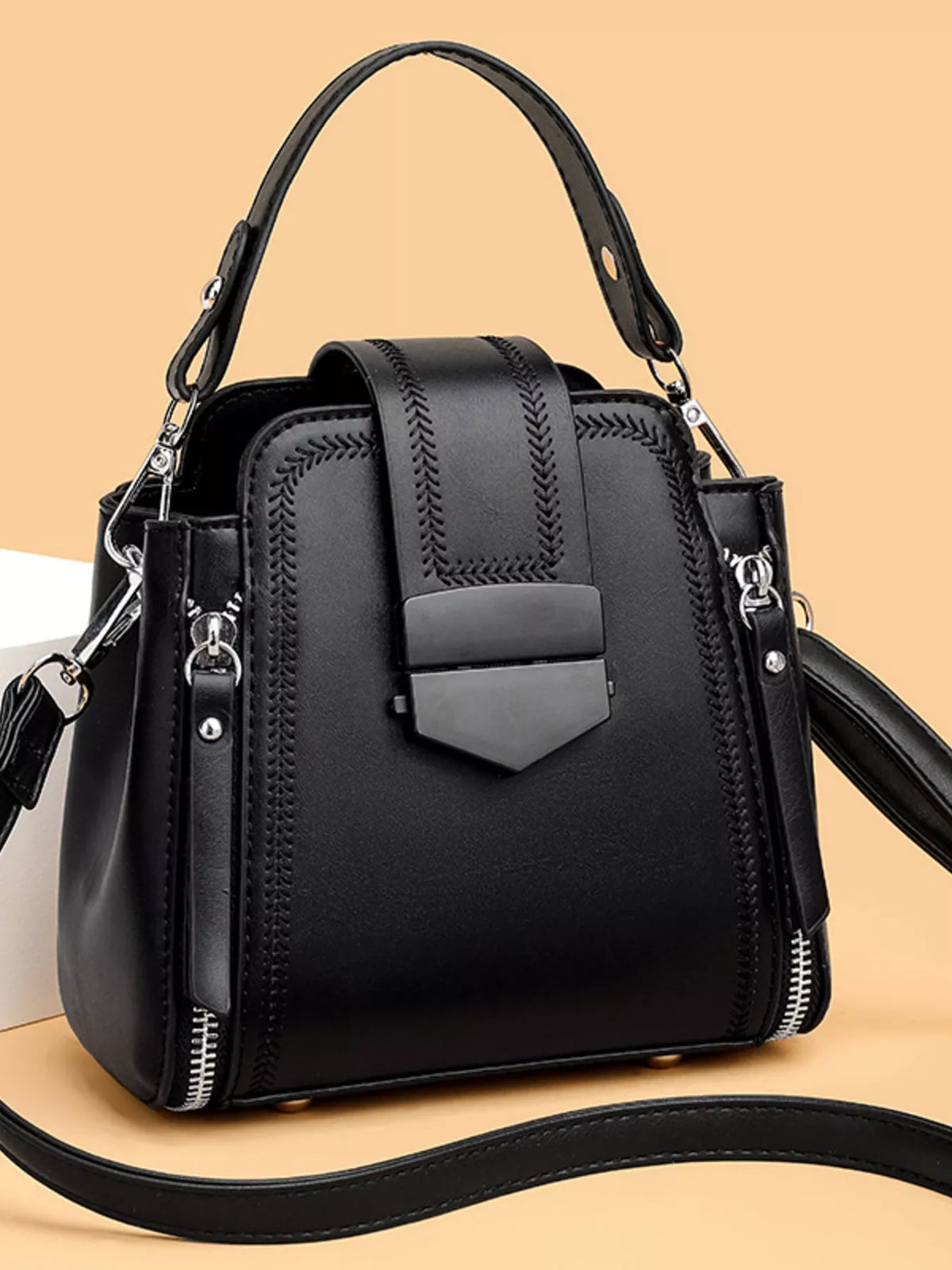 Black medium PU leather bucket crossbody bag with a structured silhouette, top handle, detachable strap, decorative stitching, flap closure, and side zippers.