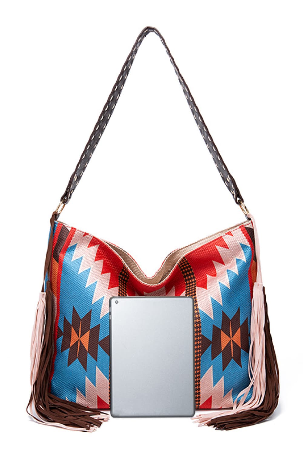Oversize geometric canvas tote bag in red, blue, white, and brown, featuring a long woven shoulder strap and fringe detailing along the sides and bottom.