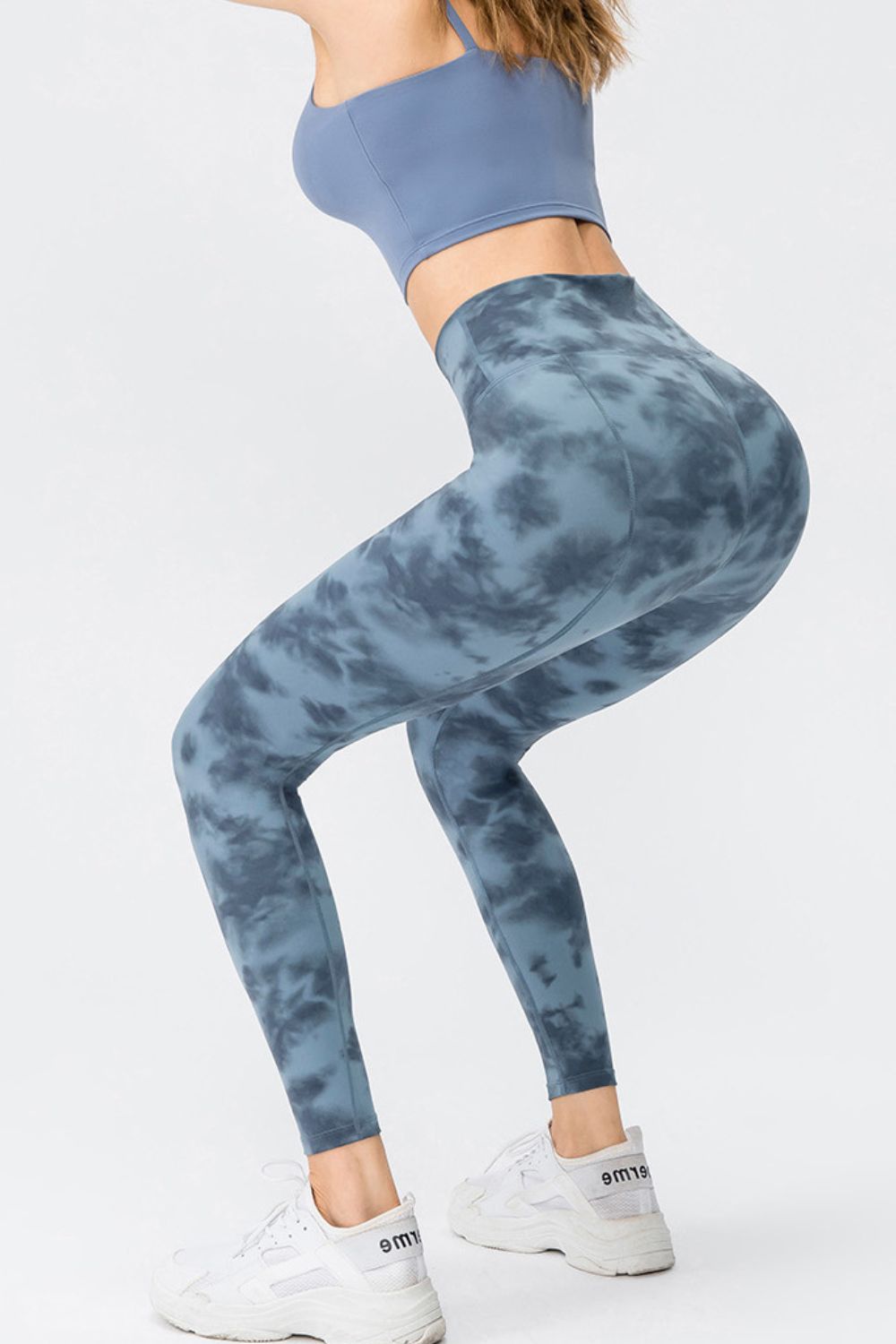 Model poses in a bent stance wearing blue-gray tie-dye slim-fit long sports leggings with a wide waistband and visible curved seam construction.