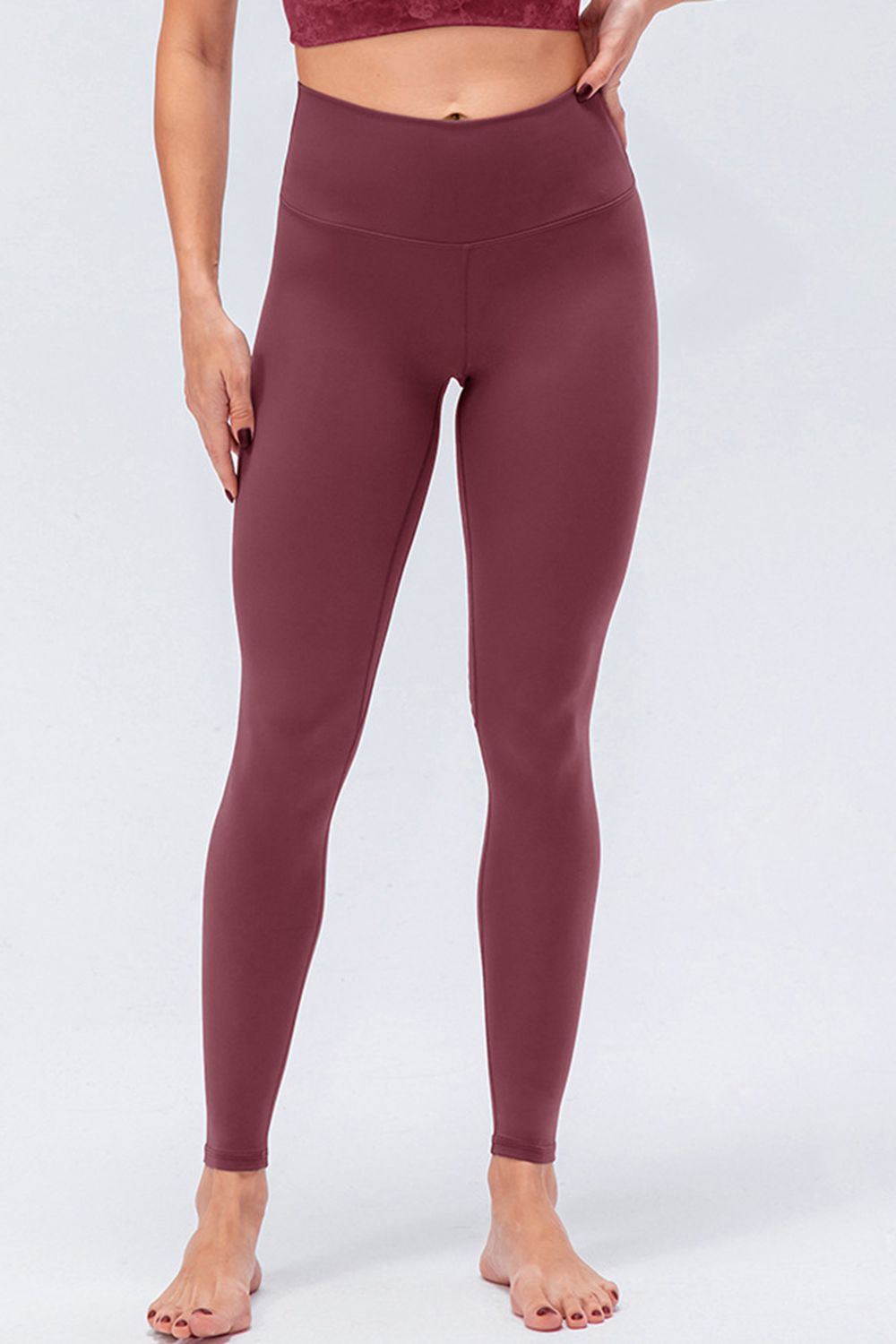 Model wearing burgundy wide-waistband slim-fit active leggings with a high-rise silhouette, smooth construction, and tapered full-length legs.
