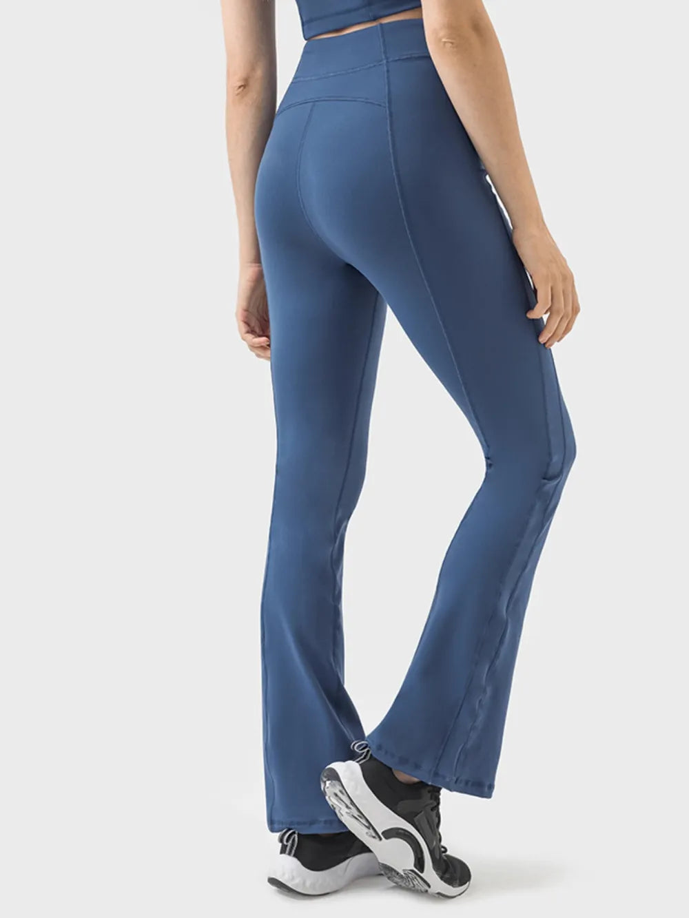 Model poses in navy blue high-waist active pants with a fitted silhouette, paneled seams, flared legs, and visible ankle zipper details.