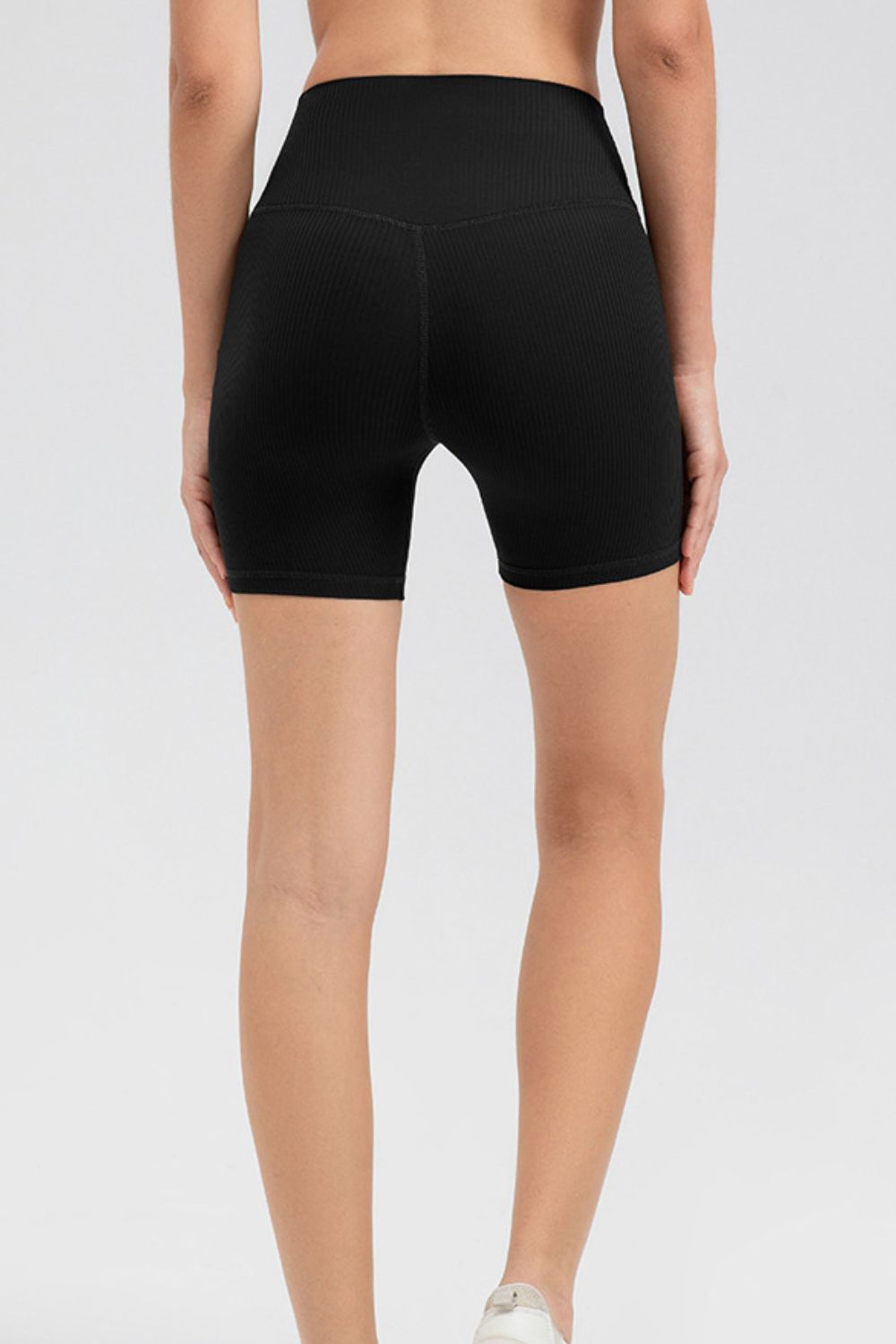 A model wears black solid slim-fit sports shorts with a wide waistband, mid-thigh silhouette, and visible center-back seam.