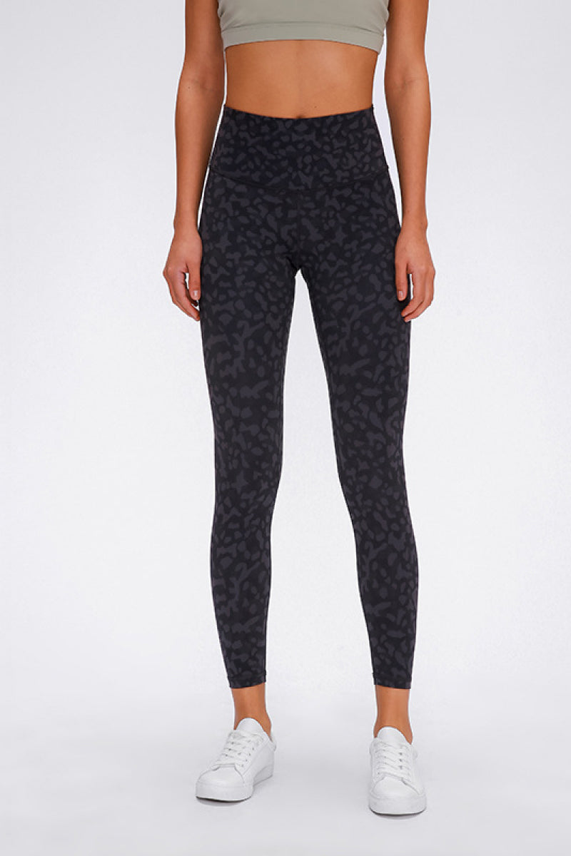 Model stands in dark patterned sports leggings featuring a wide seamless band waist, high-rise fit, and sleek ankle-length silhouette.