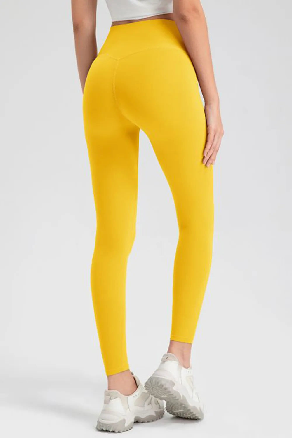 Model shown from behind wearing bright yellow high-waist skinny active pants with a close-fitting legging silhouette and visible seams.