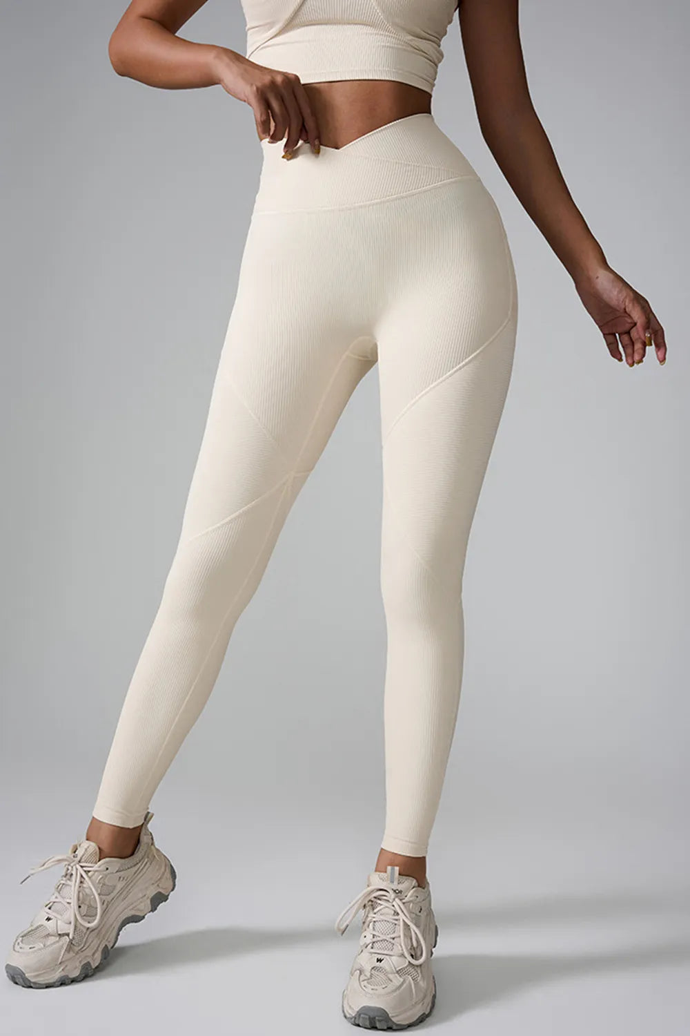 Model wearing cream high waist active leggings with a fitted full-length silhouette, ribbed stretch fabric, and diagonal seam detailing, standing in sneakers.