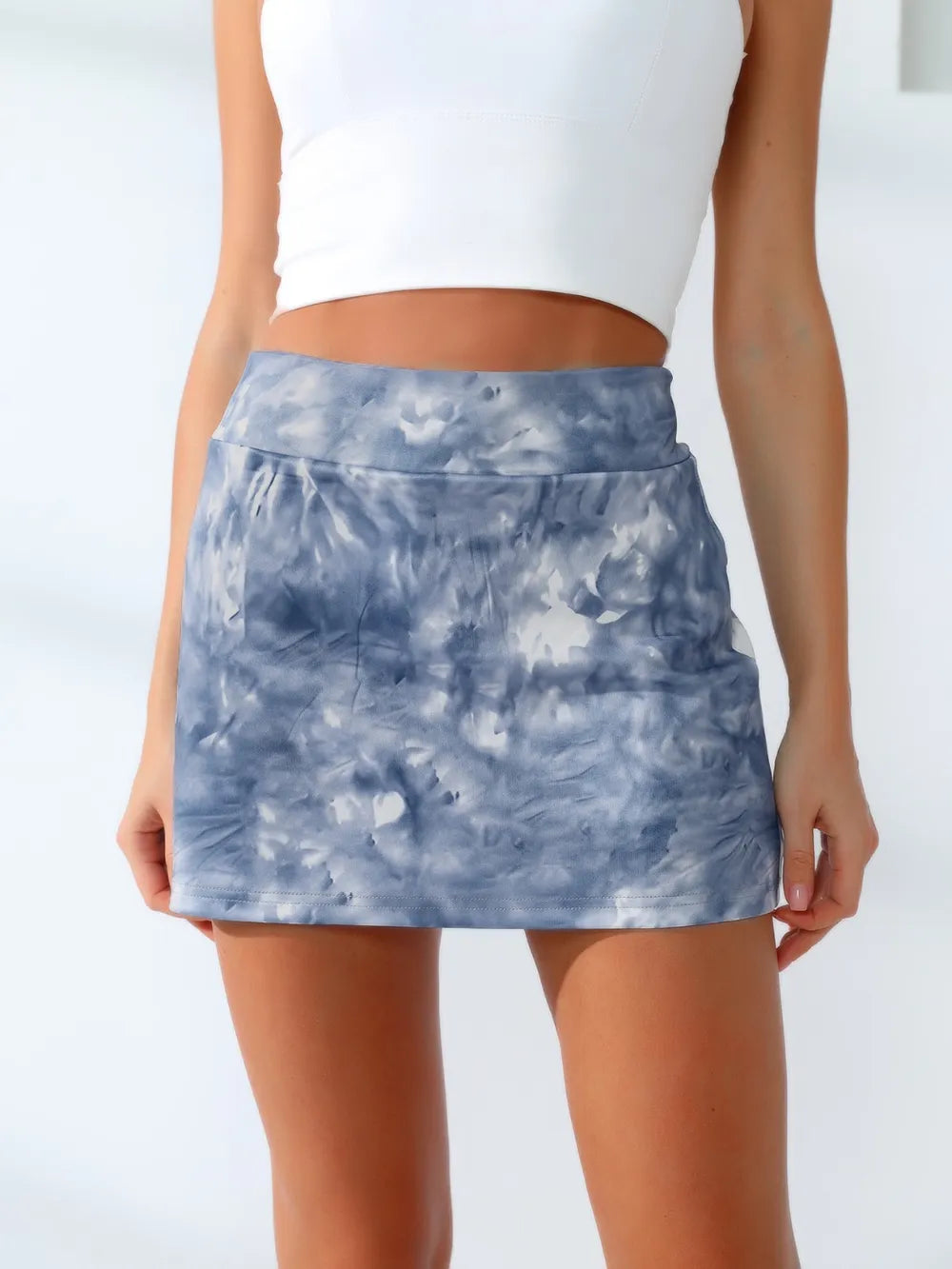 A standing model wears a blue-gray tie-dye active tennis skort with a wide waistband, straight short silhouette, and neatly stitched hem.