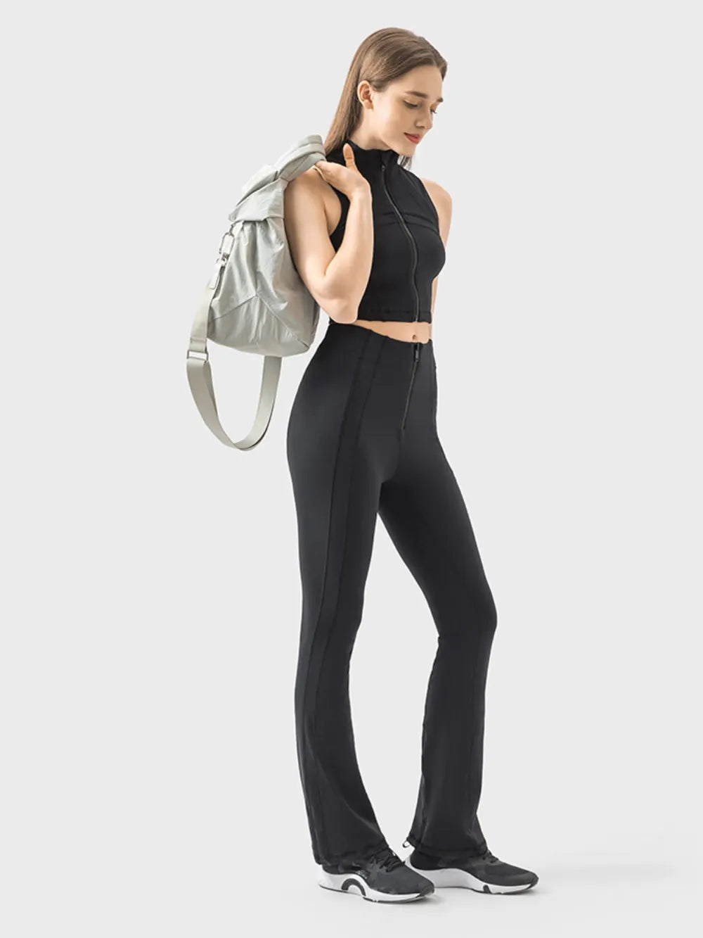 Model poses in black zipper detail high waist active pants with a sleek, slim-fitting silhouette, stretch construction, and full-length tapered legs.