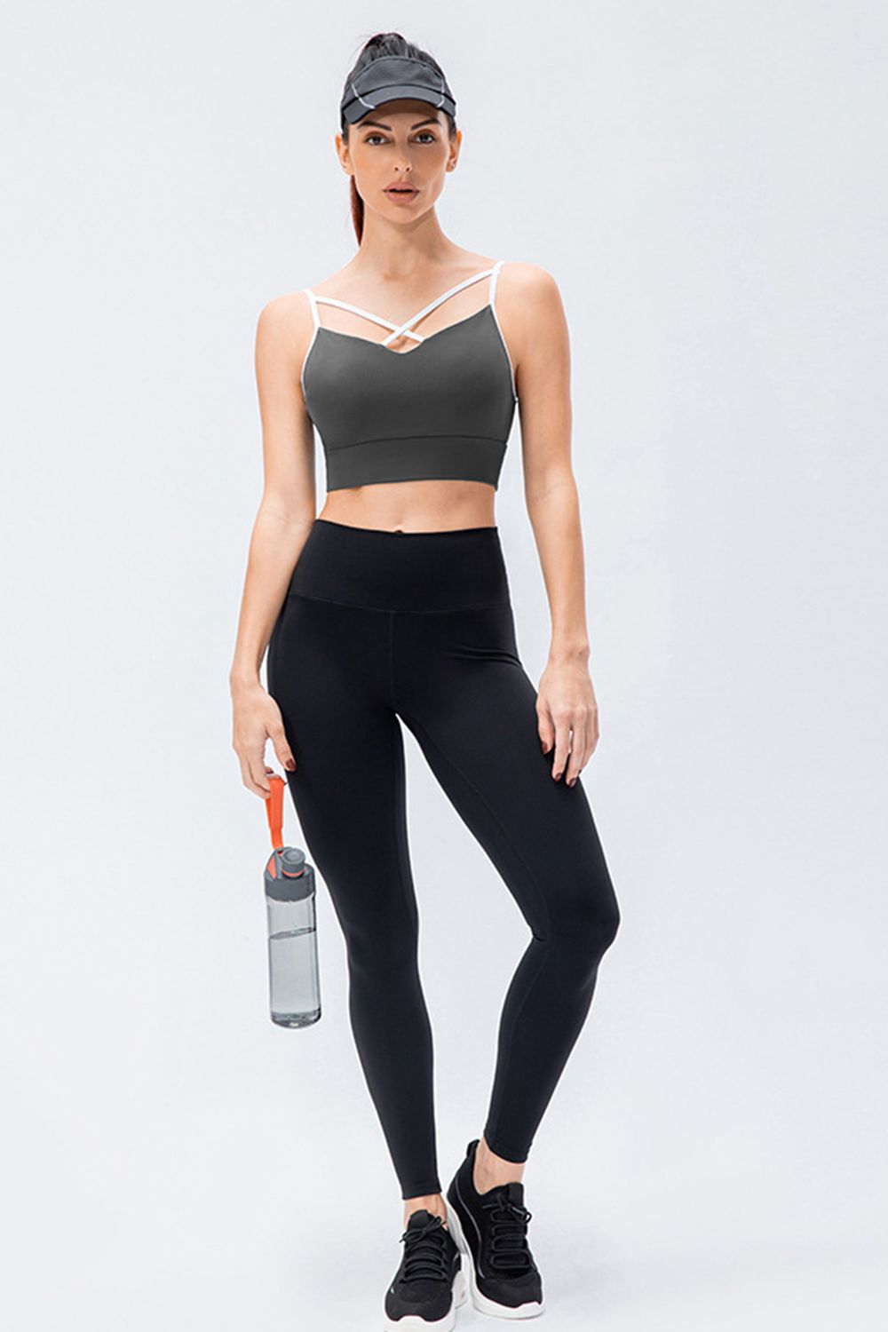 A model poses in solid black slim-fit active leggings with a wide waistband and tapered silhouette, standing with crossed legs while holding a water bottle.