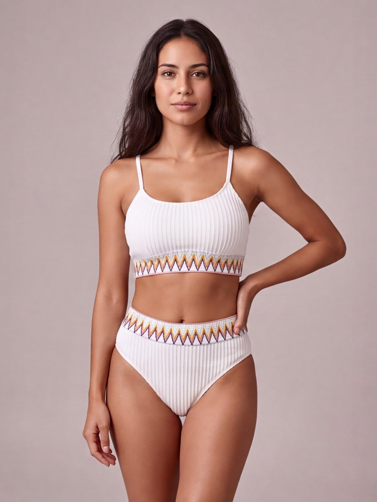 Model wears a white textured ribbed bikini with a strappy crop top and high-waist bottoms, both finished with colorful contrast zigzag banding.