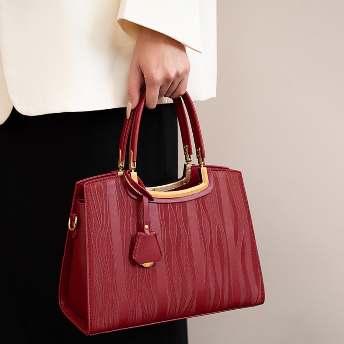 A model holds a medium burgundy crocodile-embossed PU leather top-handle handbag with a structured silhouette, dual handles, gold-toned hardware, and hanging tag.