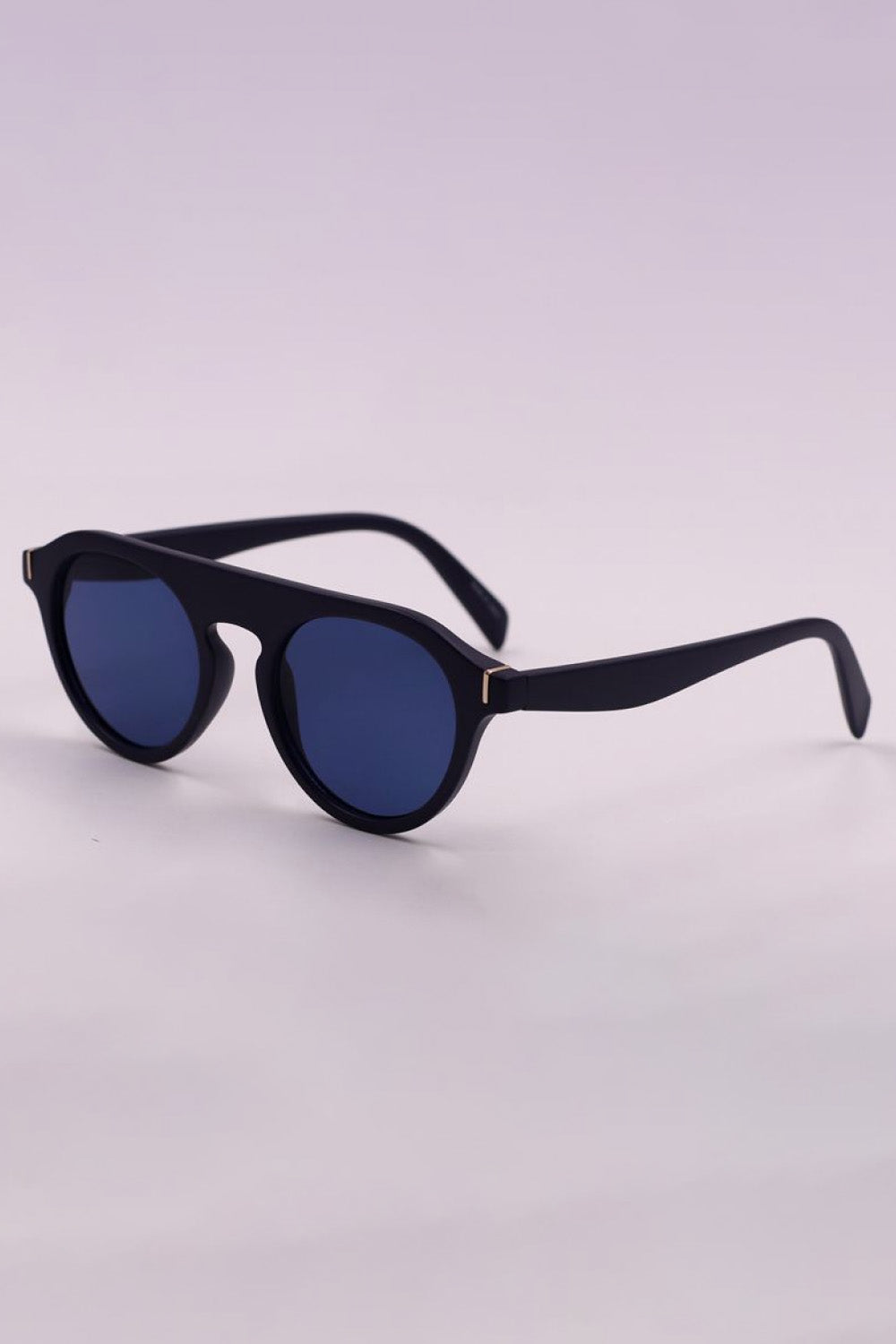 Black round full-rim polycarbonate sunglasses feature dark blue lenses, softly curved temples, and subtle gold-tone accents at the hinges.