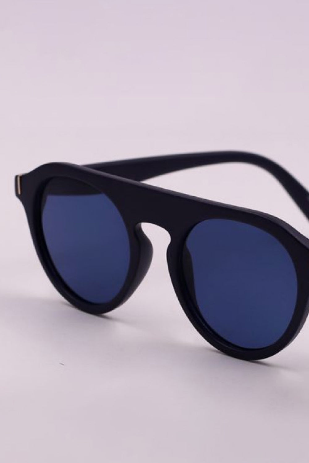 Black round full-rim sunglasses feature bold polycarbonate frames, dark blue lenses, a curved bridge, and wide temples for a vintage-inspired silhouette.