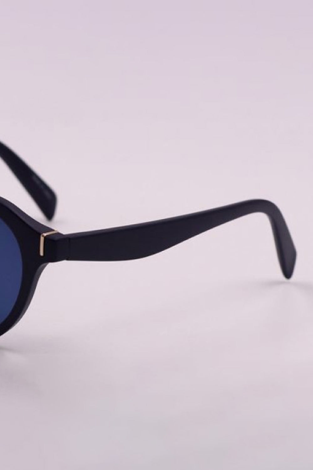 Close-up of black round full-rim sunglasses showing the polycarbonate frame, curved temple, dark lens edge, and gold-tone hinge detail.
