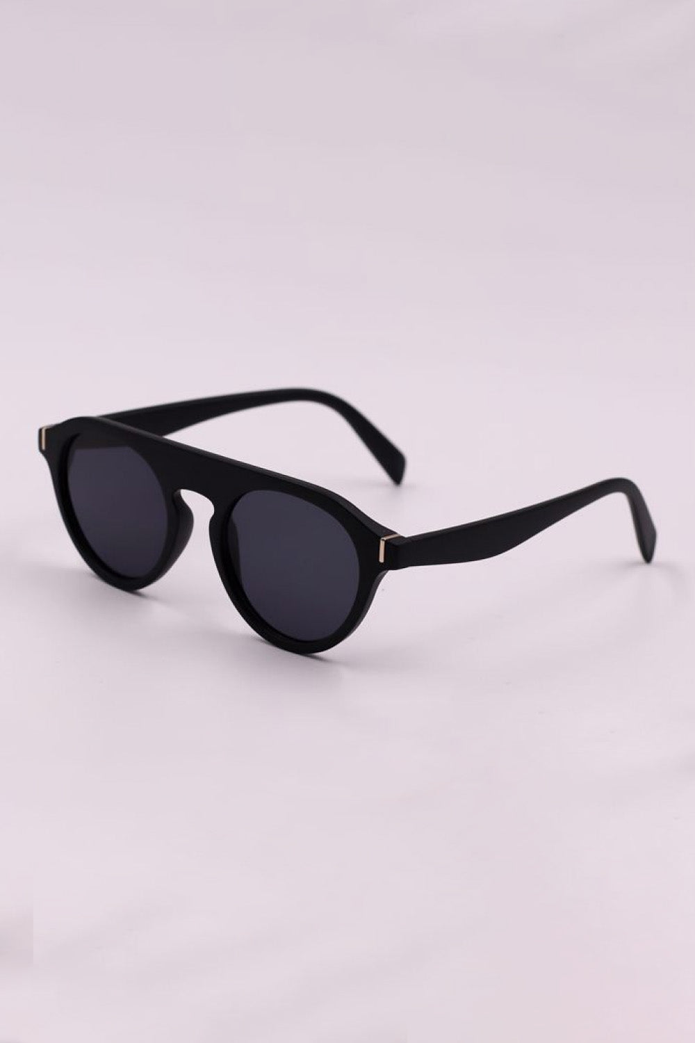 Black round full-rim sunglasses feature dark lenses, a softly curved polycarbonate frame, wide temples, and subtle gold-tone accents at the hinges.