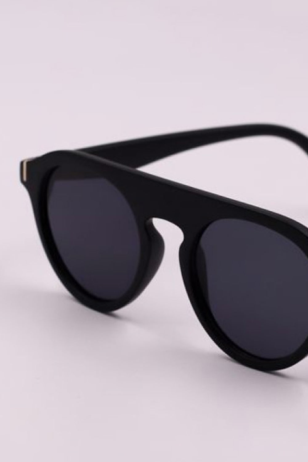 Close-up of black round full-rim sunglasses with dark lenses, a softly curved polycarbonate frame, and wide temples for a vintage-inspired silhouette.
