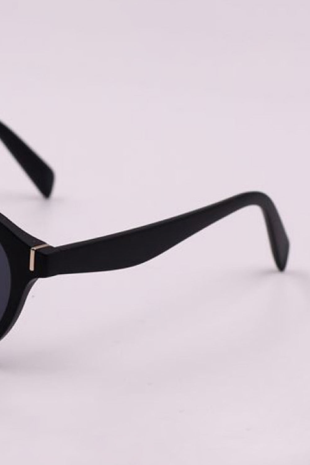 Black round full-rim sunglasses with dark lenses, tapered polycarbonate temples, curved ear pieces, and a subtle gold-tone hinge accent.