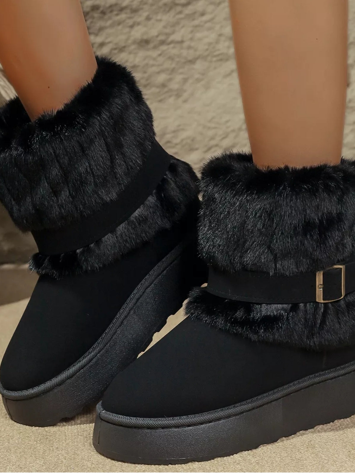 Model wears black round toe platform boots with plush faux-fur cuffs, wraparound buckle straps, low heels, and thick rubber soles.