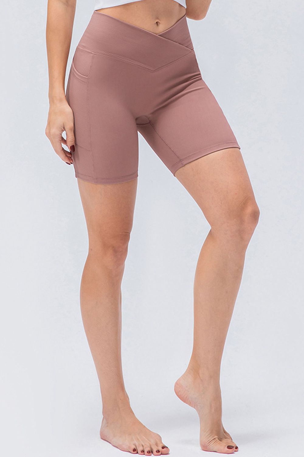 Model wearing mauve slim-fit sports shorts with a V-waistband, fitted knee-length silhouette, side pocket, and stretch construction.
