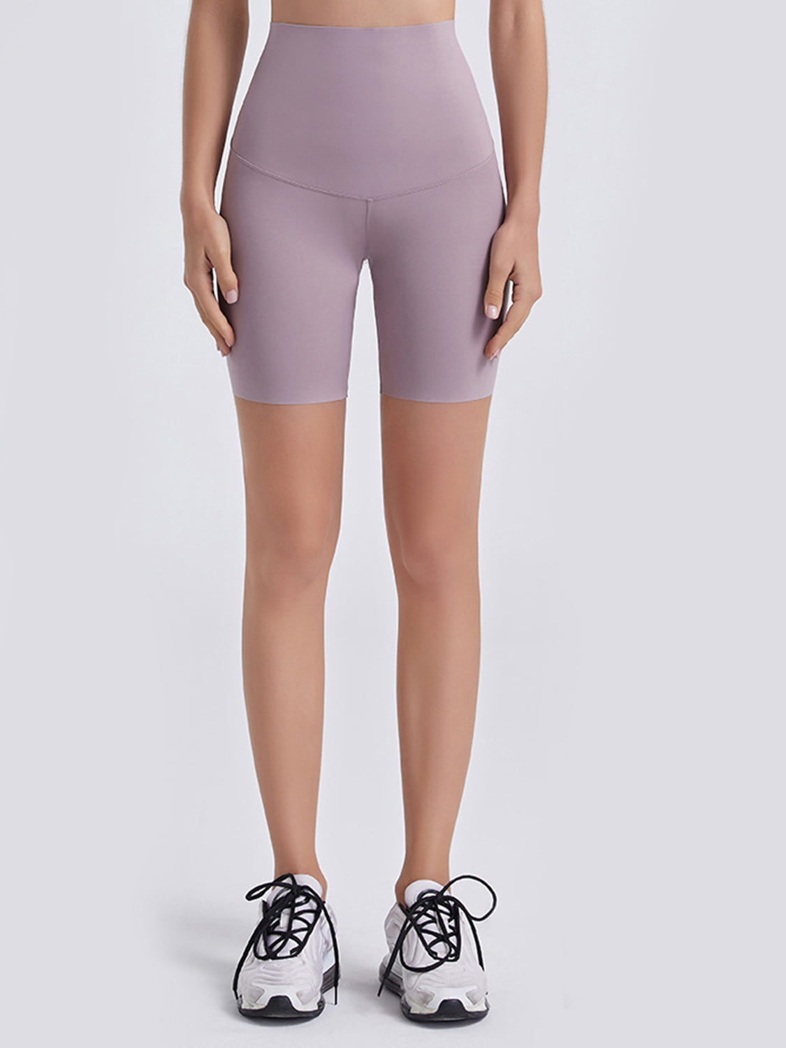 Model stands facing forward in lavender wide-waistband sports shorts with a fitted, stretchy bike-short silhouette and curved front seam.