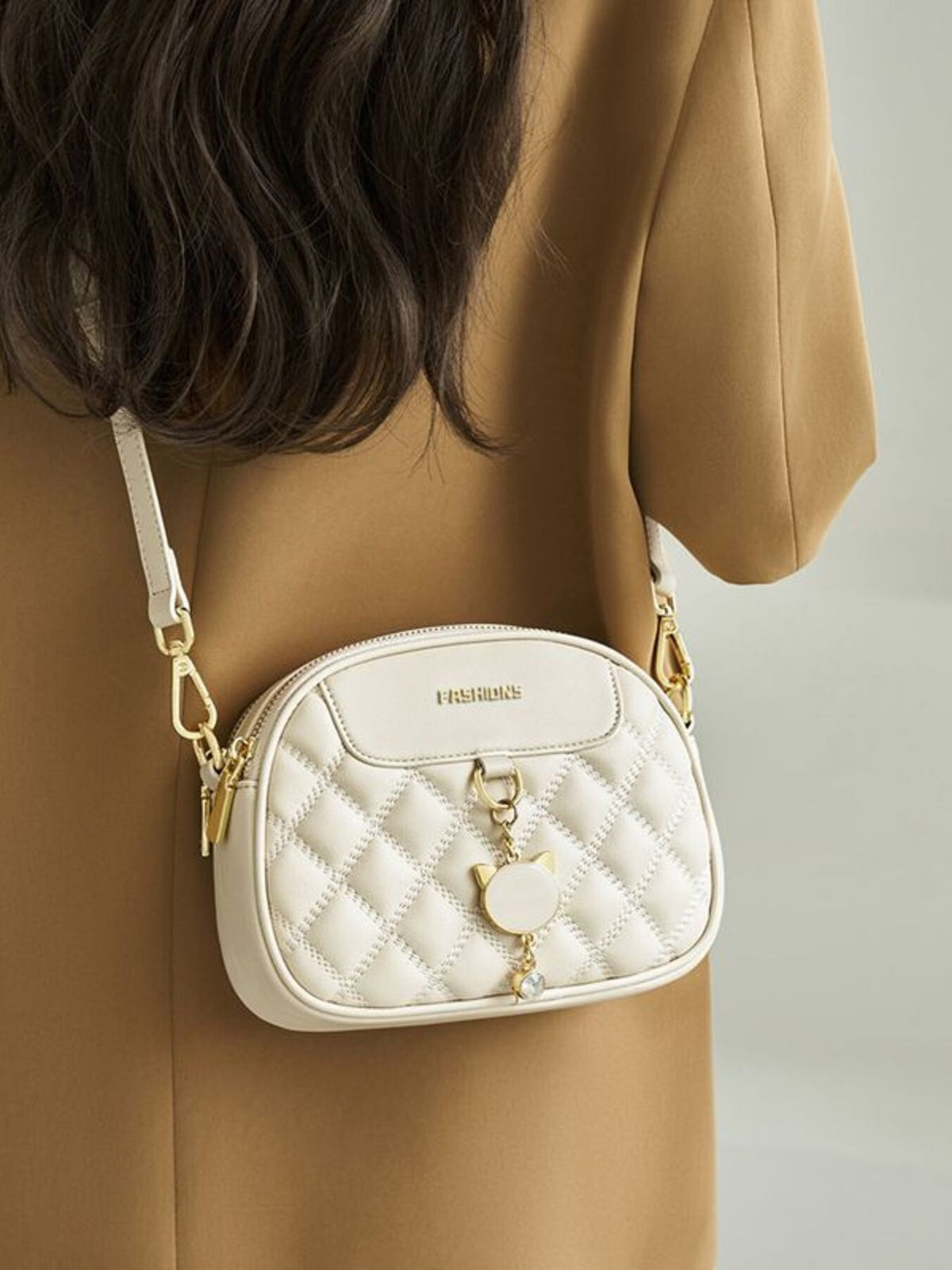 A model wears a mini white quilted PU leather crossbody bag with a rounded silhouette, gold-tone hardware, and decorative front charm.
