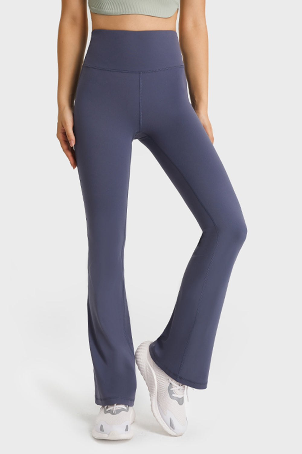A model wears dark navy elastic-waist flare yoga pants with a high waistband, smooth fitted silhouette, visible seams, and long flared hems while standing with one leg crossed.
