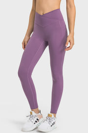 A model wears purple V-waist yoga leggings with a fitted silhouette, visible side pocket, and streamlined seam detailing along the legs.