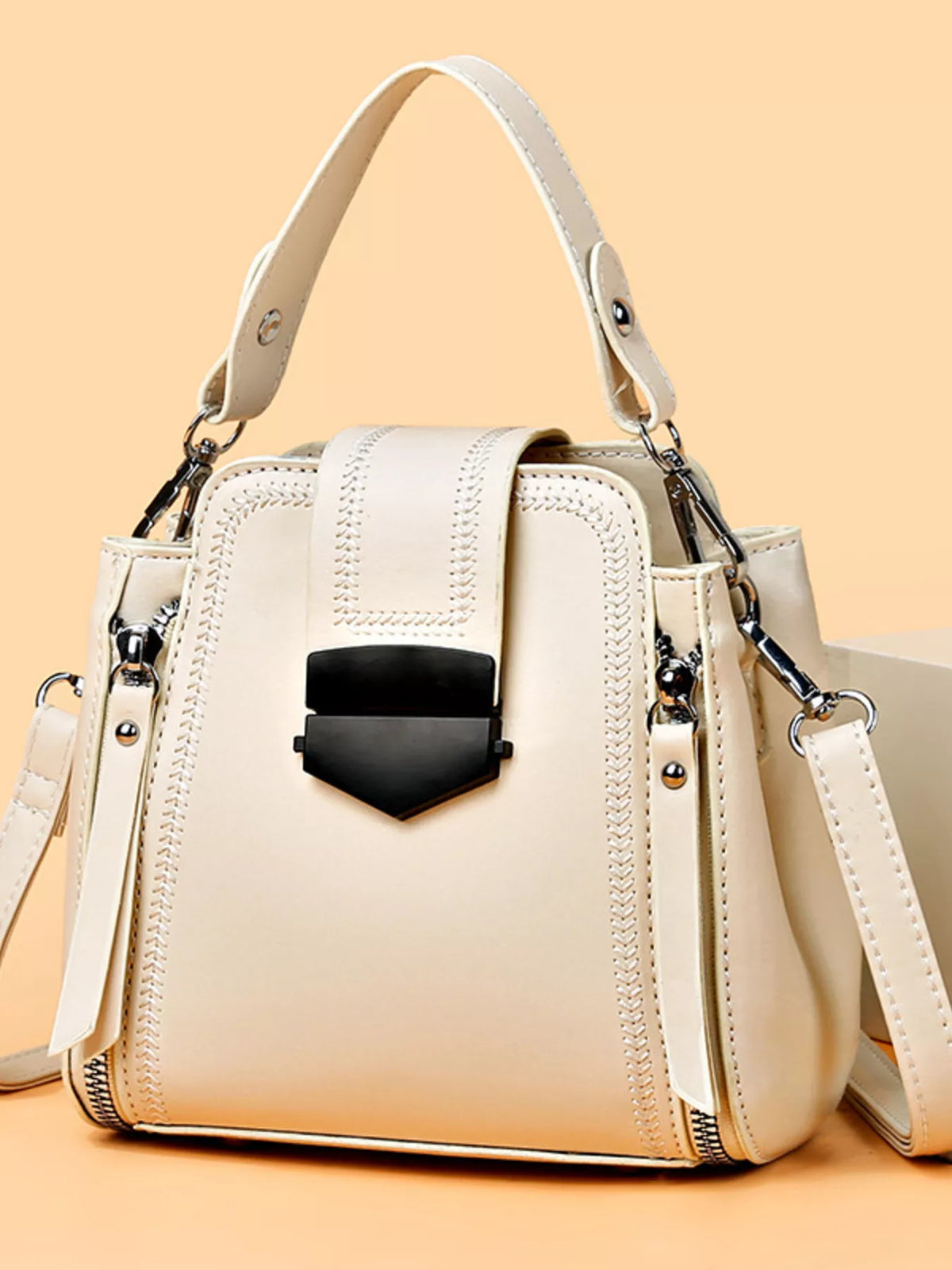 A medium cream PU leather bucket crossbody bag with a structured silhouette, decorative stitching, flap closure, black clasp, top handle, and detachable strap.