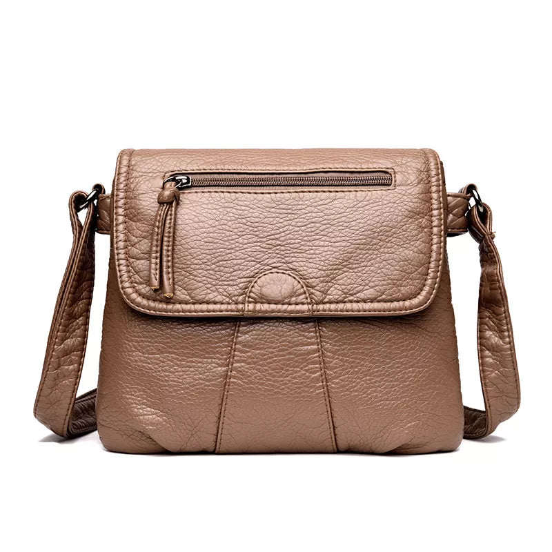 Small taupe PU leather crossbody bag with an adjustable strap, flap closure, front zip pocket, stitched panels, and a structured rectangular silhouette.